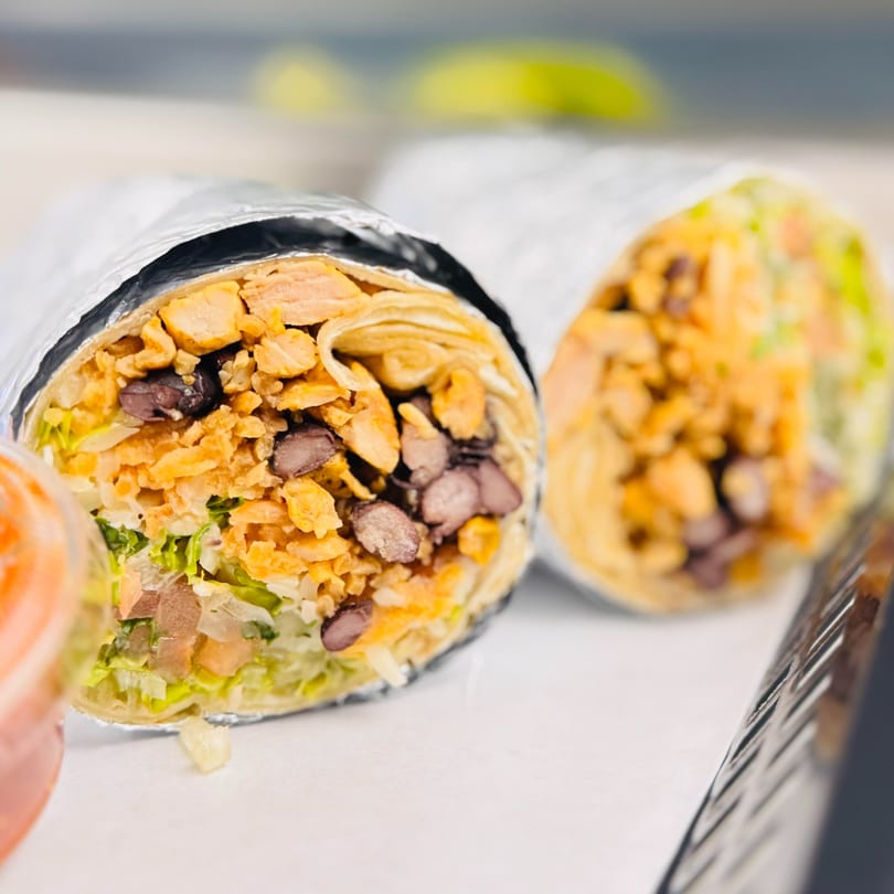 Two large burritos, one cut open to reveal chicken, black beans, lettuce, and crispy toppings.
