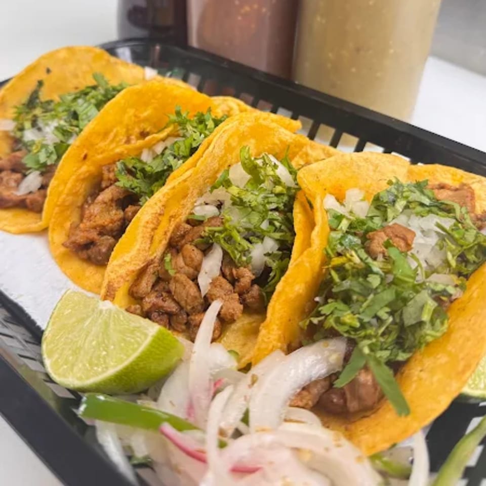 Three HP Taco Shop tacos with meat, cilantro, and onions, served with lime and sliced onions.