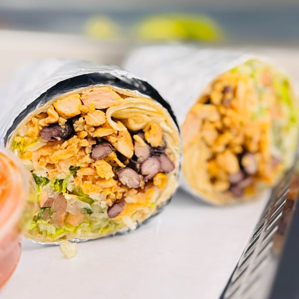 Two large burritos, one cut open to show chicken, black beans, rice, and lettuce.